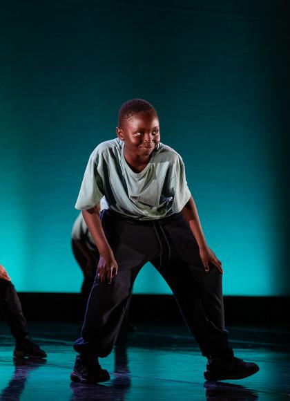 Young people dancing on a black stage against a blue-lit background