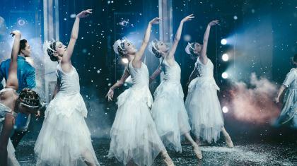 Four female dancers dressed in white each extending a foot down and an arm high