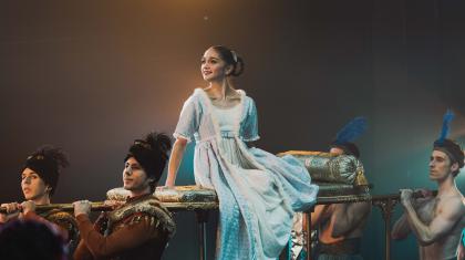 A young woman on a sedan chair held aloft on the shoulders of four dancers