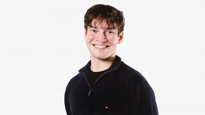 Wearing a black fleece jacket, a man smiles broadly at the camera, he has short brown hair