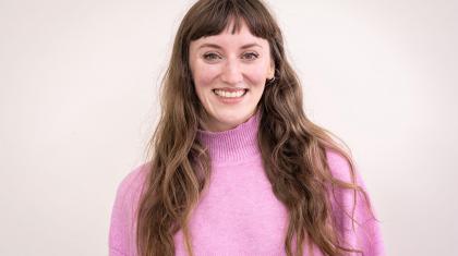 Woman in a pink turtle-neck sweater, long brown hair with a fringe, smiling warmly