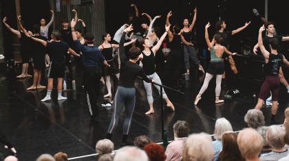 Company class with dancers at the barre while supporters watch