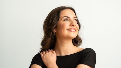 Woman with long, dark hair and a black T-shirt, smiling while looking upward and one of her hands on a shoulder