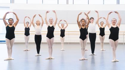 Students in a class, all with their hands above their heads, knees and ankles together