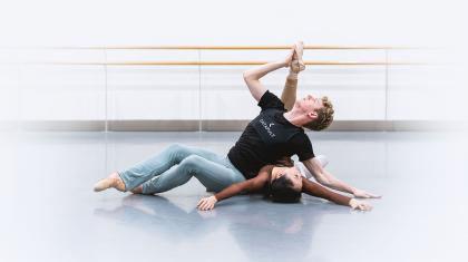 On the studio floor a female dancer lies back, a male dancer leans against her torso